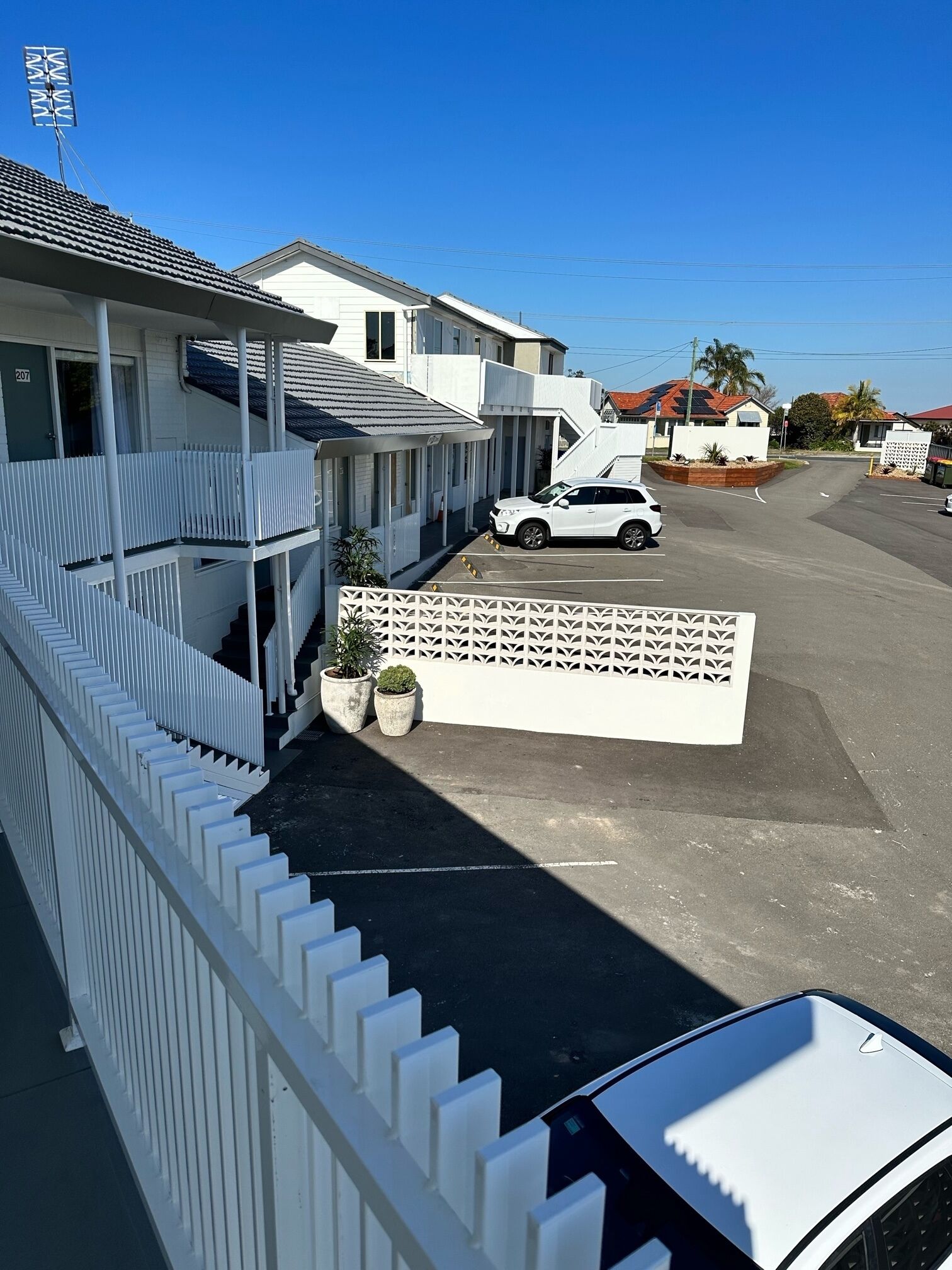 A residential area with a white house, a white car parked in front, and a white fence.