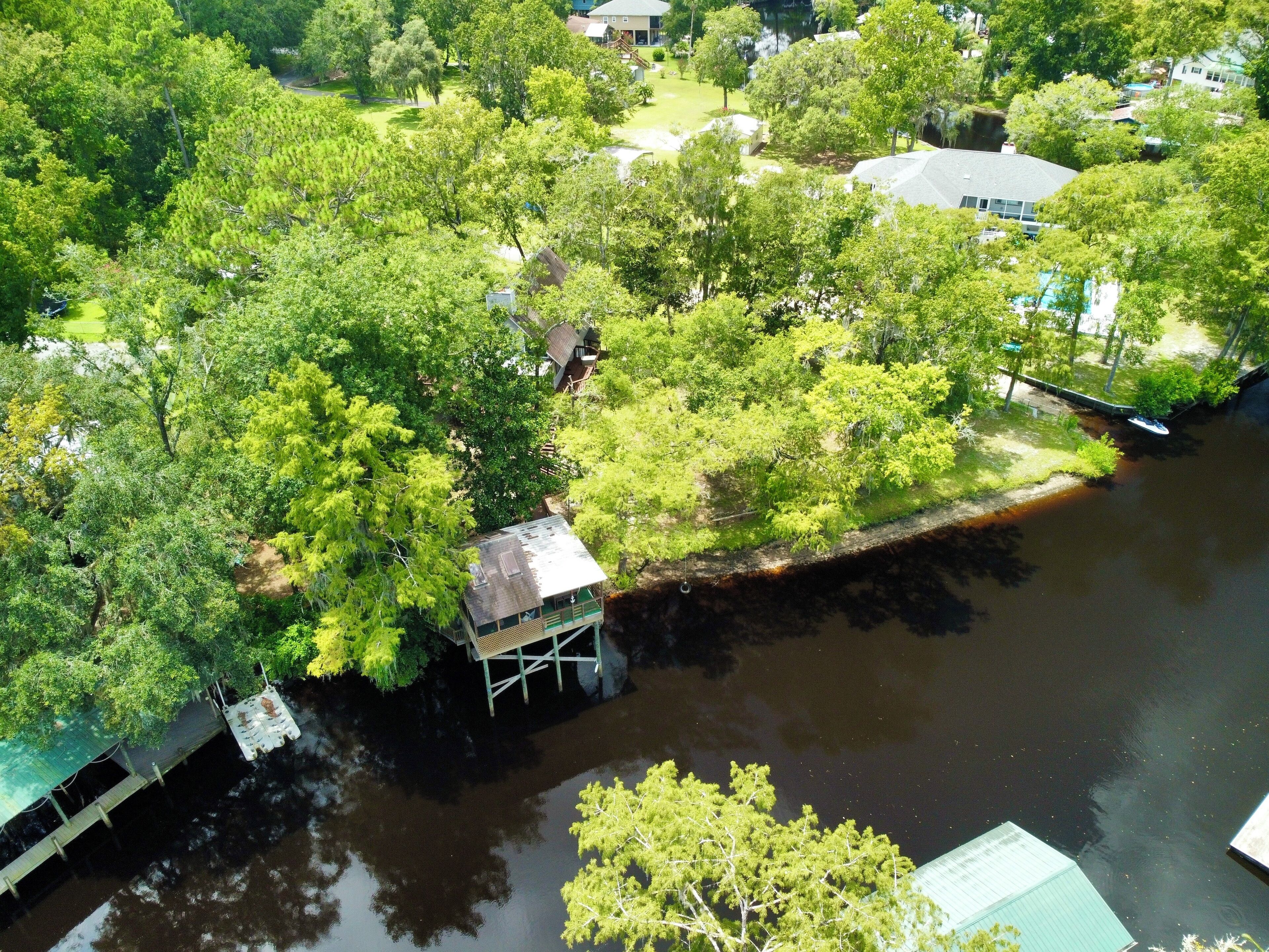 An aerial view of a riverside property with a dock, a small wooden structure, and lush greenery.