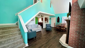 A spacious living area with a staircase, a dining table, and a kitchen in the background.