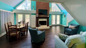 A spacious living room with a fireplace, a dining area with wooden chairs, and a large window providing natural light.