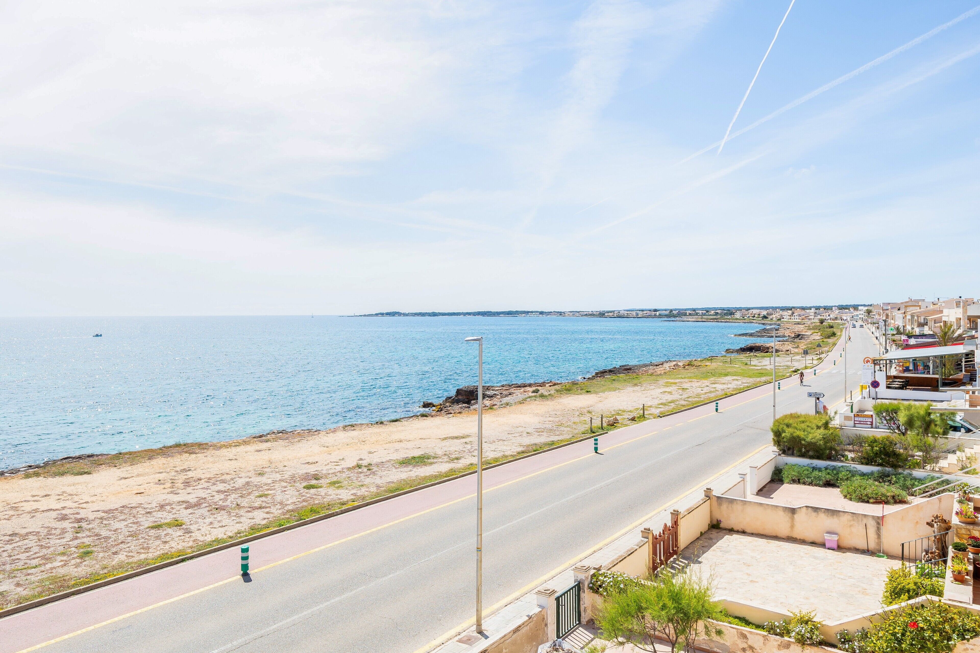 Una carretera costera con vistas despejadas al mar, un sendero peatonal y edificios con balcones.