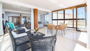 A spacious living area with wicker furniture, a dining table, and large windows offering a view of the outside. - Apartment 'Brisas Vista Mar' with Sea View, Wi-Fi and Air Conditioning (Sa Ràpita)
