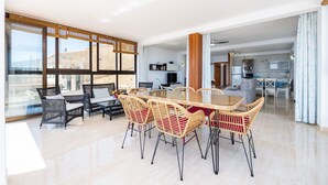 A spacious living area with a large dining table, wicker chairs, a sofa, and a kitchen in the background. - Apartment 'Brisas Vista Mar' with Sea View, Wi-Fi and Air Conditioning (Sa Ràpita)