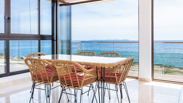 A dining area with a table and chairs, large windows, and a view of the sea. - Apartment 'Brisas Vista Mar' with Sea View, Wi-Fi and Air Conditioning (Sa Ràpita)