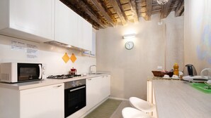 A modern kitchen with white cabinets, a microwave, stove, and a sink. There are two white chairs and a green rug. - Vacation Home "Ca' Lirica" with Wi-Fi & A/C (Venezia)