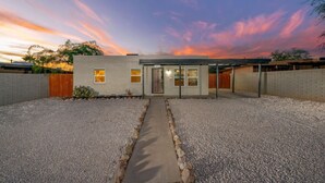A modern house with a gravel driveway, a covered patio, and a view of the sunset. - Central / Remodeled / Fenced / Clean / 3 BR 2 BA (Tucson)