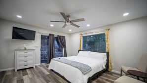 A bedroom with a bed, a TV, a ceiling fan, and a window with curtains. - Four bedroom with hot tub and views! (Kerrville)
