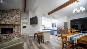A modern kitchen with a stone fireplace, wooden dining table, and bar stools. - Four bedroom with hot tub and views! (Kerrville)