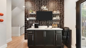 A modern kitchen with dark cabinets, a black countertop, and a neon sign above the TV. - ★ HostWise Stays ★ Luxe Hot Tub | Great Patio | Driveway Parking (Pittsburgh)