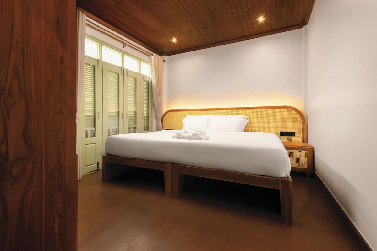 A bedroom with a wooden bed frame, white bedding, and a nightstand with a lamp.