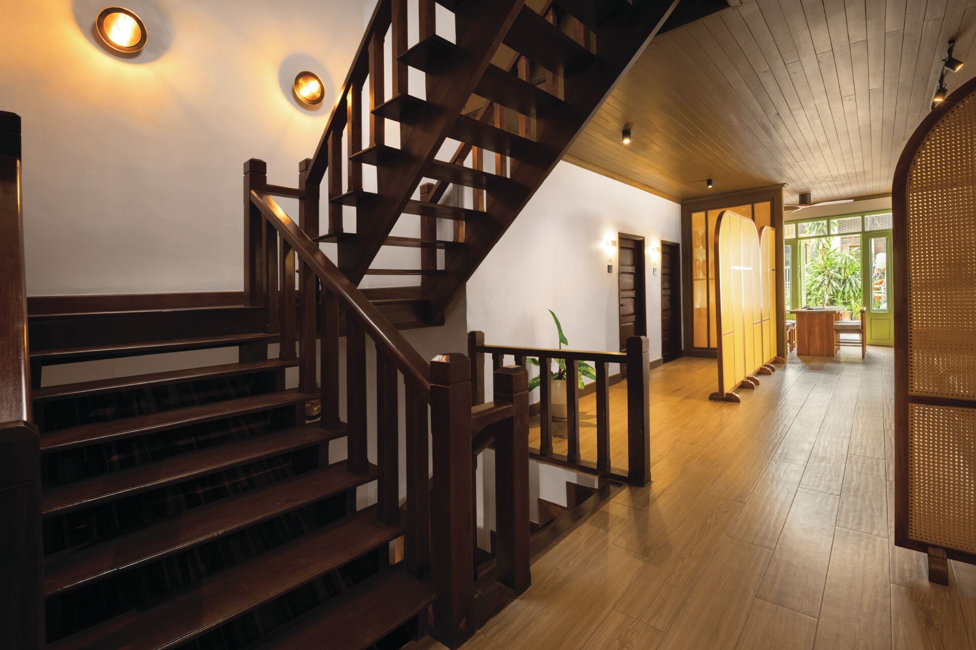 A wooden staircase with a railing, leading to a room with a large window and a plant.