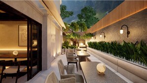 An outdoor patio area with seating and tables, surrounded by plants and a view of trees.