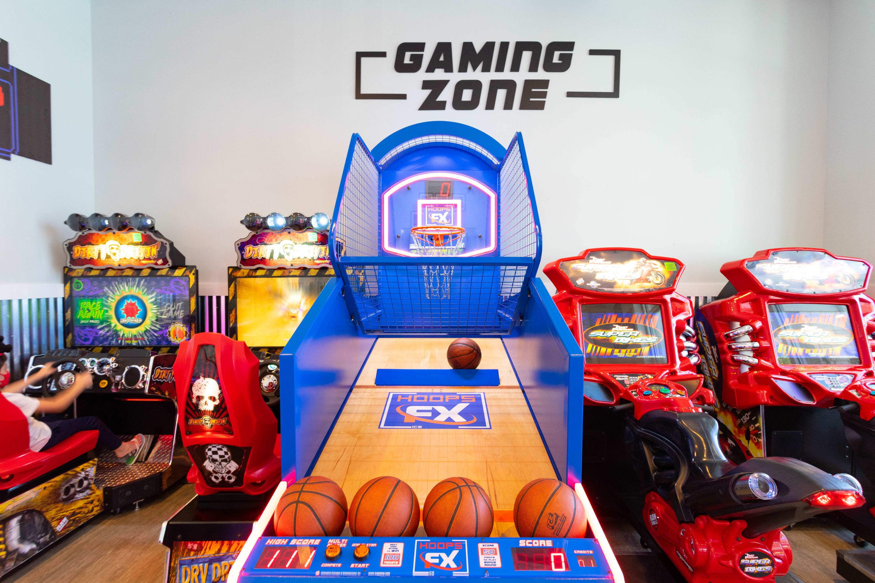 Un salón de juegos interior con un aro de baloncesto y diversas máquinas recreativas.