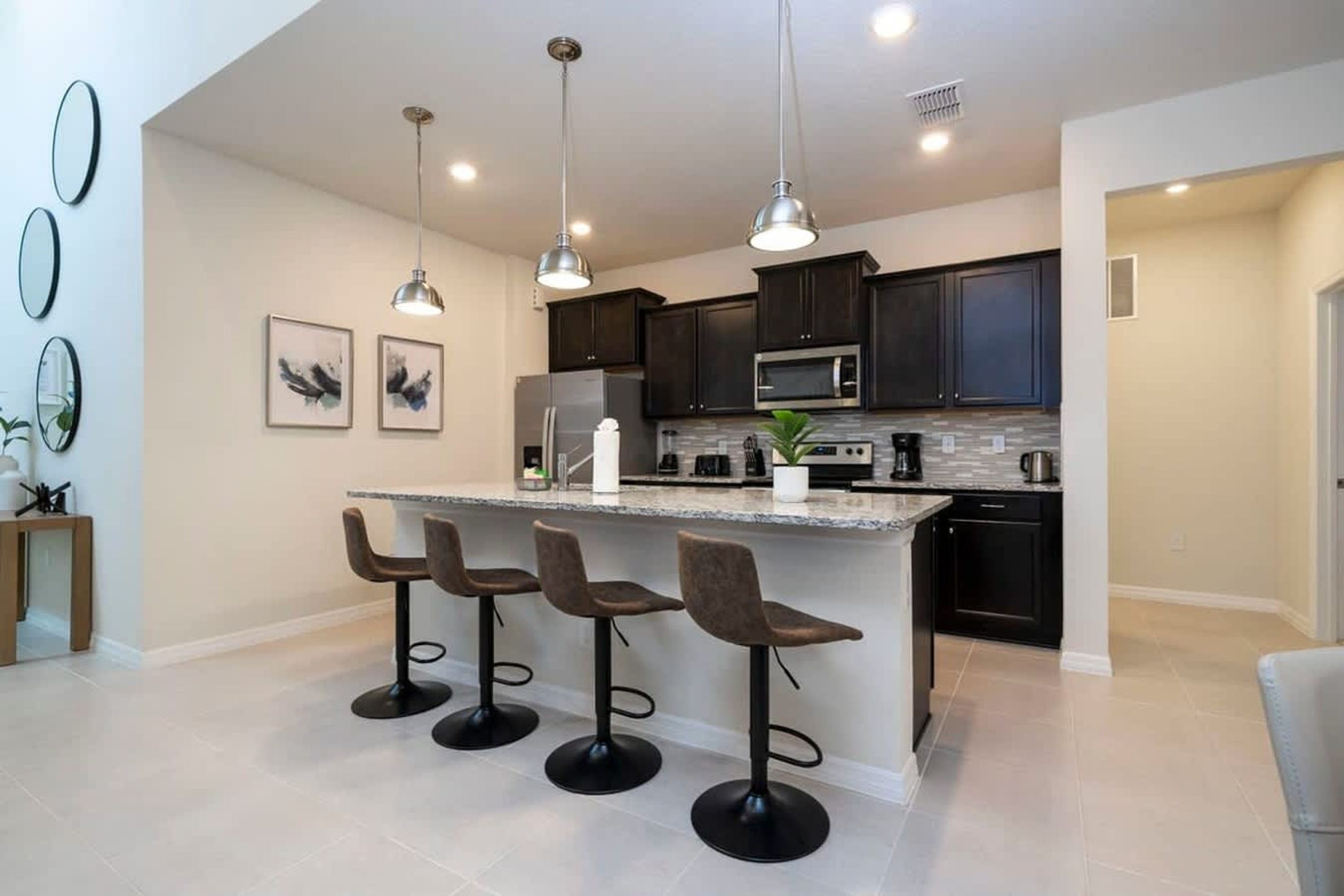 A modern kitchen with dark cabinets, a central island with bar stools, pendant lighting, and a microwave.
