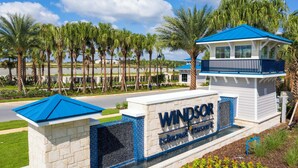 Een bord met 'Windsor Island Resort', met een blauw dak en witte muren, omringd door palmbomen en een heldere lucht.