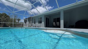 A swimming pool with a clear blue water surface, surrounded by a covered patio area with chairs and a barbecue grill. - Modern and spacious getaway with a pool and grill (Cocoa)