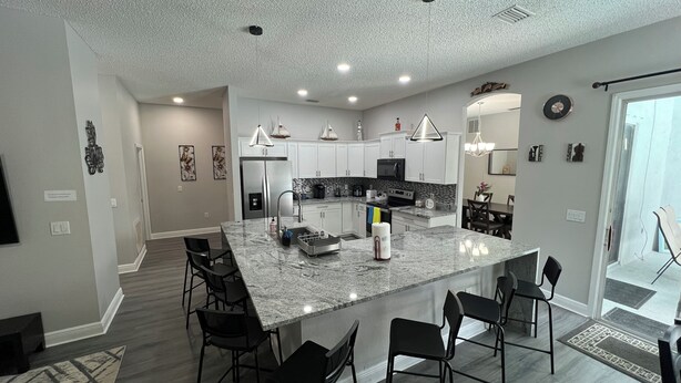 A modern kitchen with a large island, white cabinets, and a dining area with black chairs. - Modern and spacious getaway with a pool and grill (Cocoa)