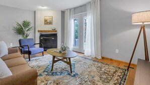 Un salon comprenant un canapé, un fauteuil, une table basse, une cheminée et une vue à travers une porte vitrée.
