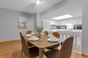 A dining area with a table set for four, a potted plant, and a kitchen in the background.