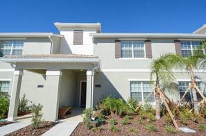 A two-story residential building with a covered porch, a small garden with palm trees, and a clear blue sky. - Private Pool, Prime Location, Beautiful Home (Kissimmee)