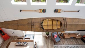 A spacious room with a large wooden canoe hanging from the ceiling, a dining table with chairs, a flag, and a small table with decorative items. - Downtown Retreat with Bikes, Fire Pit & Kayaks (Saint Michaels)