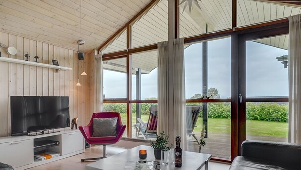 A modern living room with a TV, a red chair, a table with a bottle, and a view of the outdoors. - "Juliana" - 400m from the sea by Interhome (Nordborg)