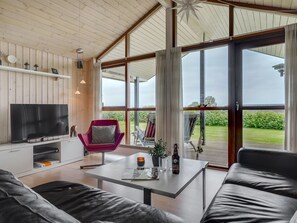 A modern living room with a TV, a red chair, a table with a bottle, and a view of the outdoors. - "Juliana" - 400m from the sea by Interhome (Nordborg)