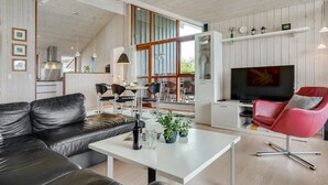 A modern living room with a black leather sofa, a white coffee table, and a red chair. There is a television on a white cabinet, and a kitchen area is visible in the background. - "Juliana" - 400m from the sea by Interhome (Nordborg)