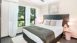 Ein modernes Hotelzimmer mit einem großen Bett, einem Deckenventilator, einem Fenster mit Vorhängen, einem Nachttisch mit Lampe und einem Wandbild.