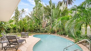 Ein Swimmingpool, umgeben von üppiger tropischer Vegetation und einem überdachten Sitzbereich mit Stühlen und einem Tisch.