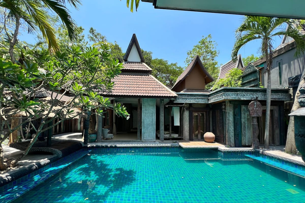 Une piscine entourée d’une architecture traditionnelle, avec une structure à toit de chaume et une zone de piscine carrelée.