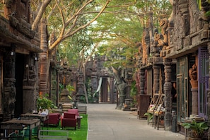 A narrow pathway flanked by intricately carved stone pillars and columns, leading to a traditional building with a wooden door. - K2 Xanadu Pool Villa (Bang Lamung)