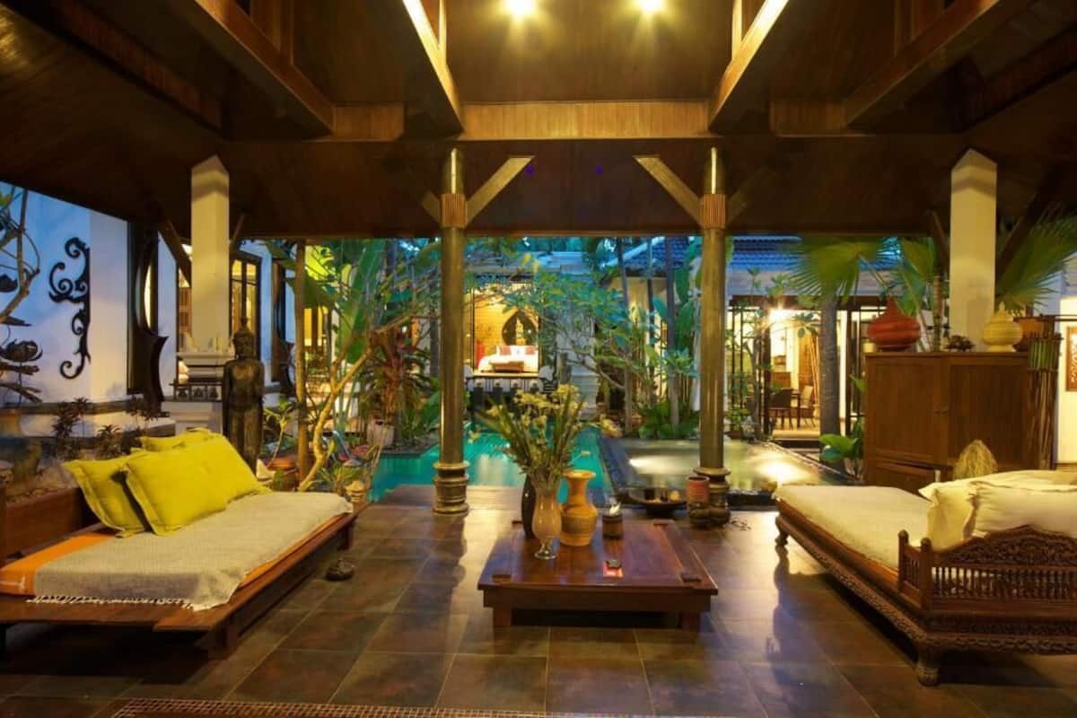 Un hall d’entrée spacieux avec une piscine, des meubles en bois et des plantes tropicales.