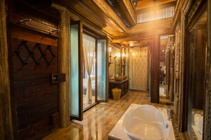A traditional wooden bathroom with a large bathtub, a wooden door, and a mirror reflecting the room. - K2 Xanadu Pool Villa (Bang Lamung)