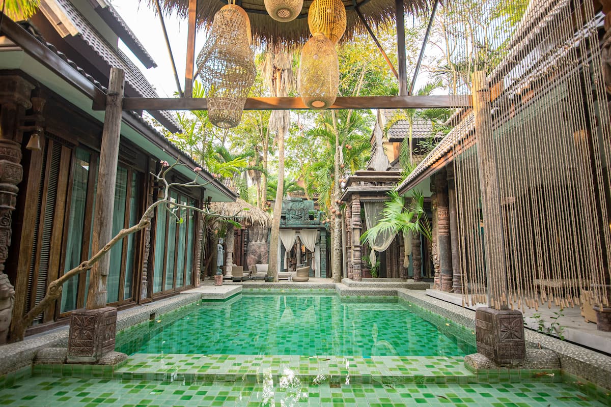 Un espace piscine traditionnel avec un sol carrelé, des piliers en bois et des lanternes suspendues.