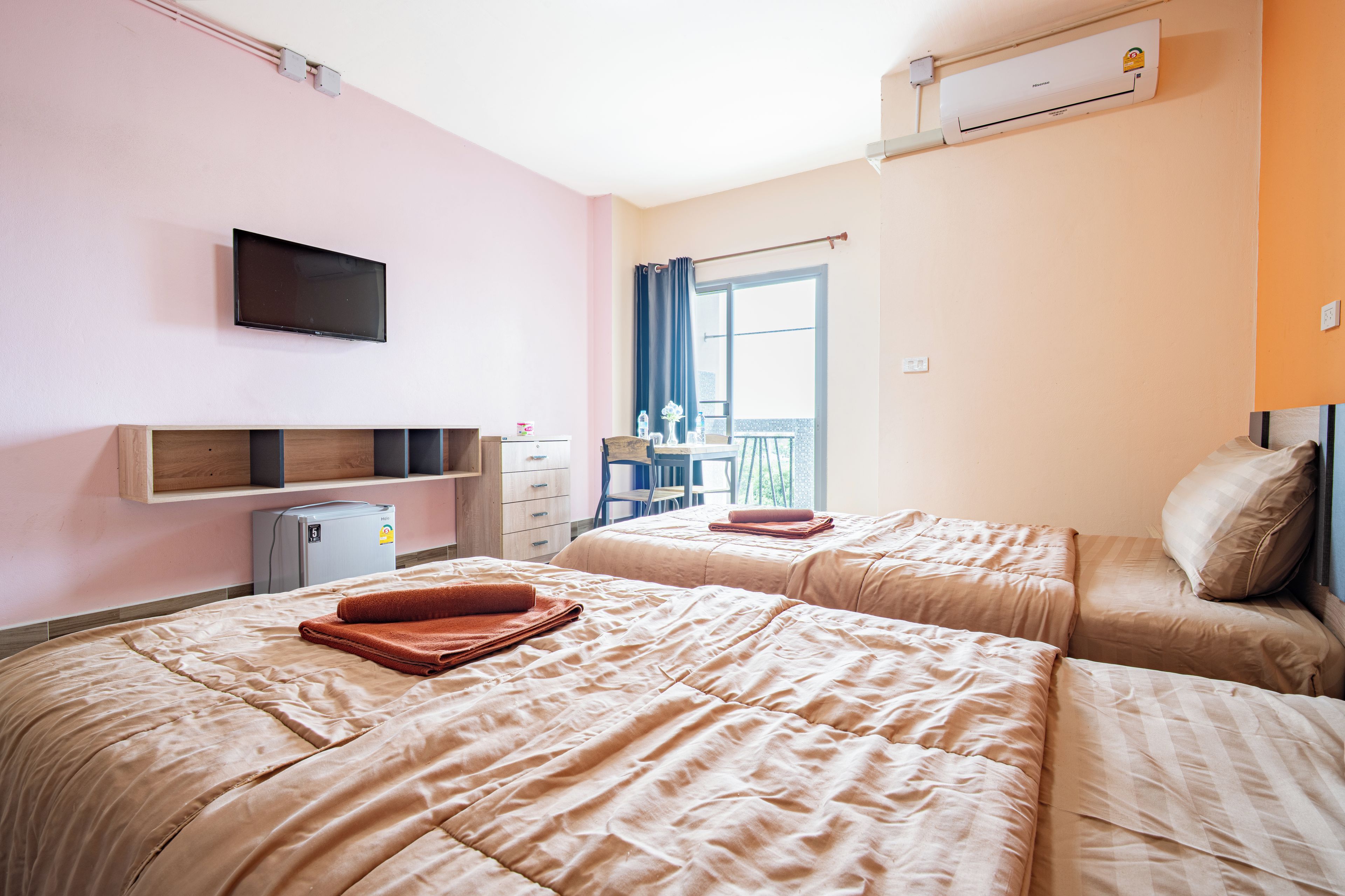 Habitación de hotel con dos camas, televisión, un refrigerador pequeño y una ventana con cortinas.