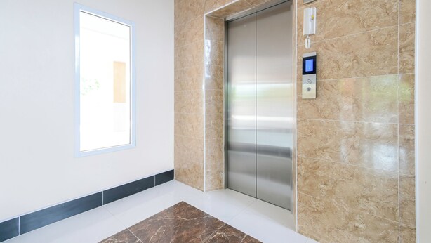A modern elevator with a digital control panel, beige marble walls, and a white floor with a brown accent strip. - The Wish Hotel (Chachoengsao)