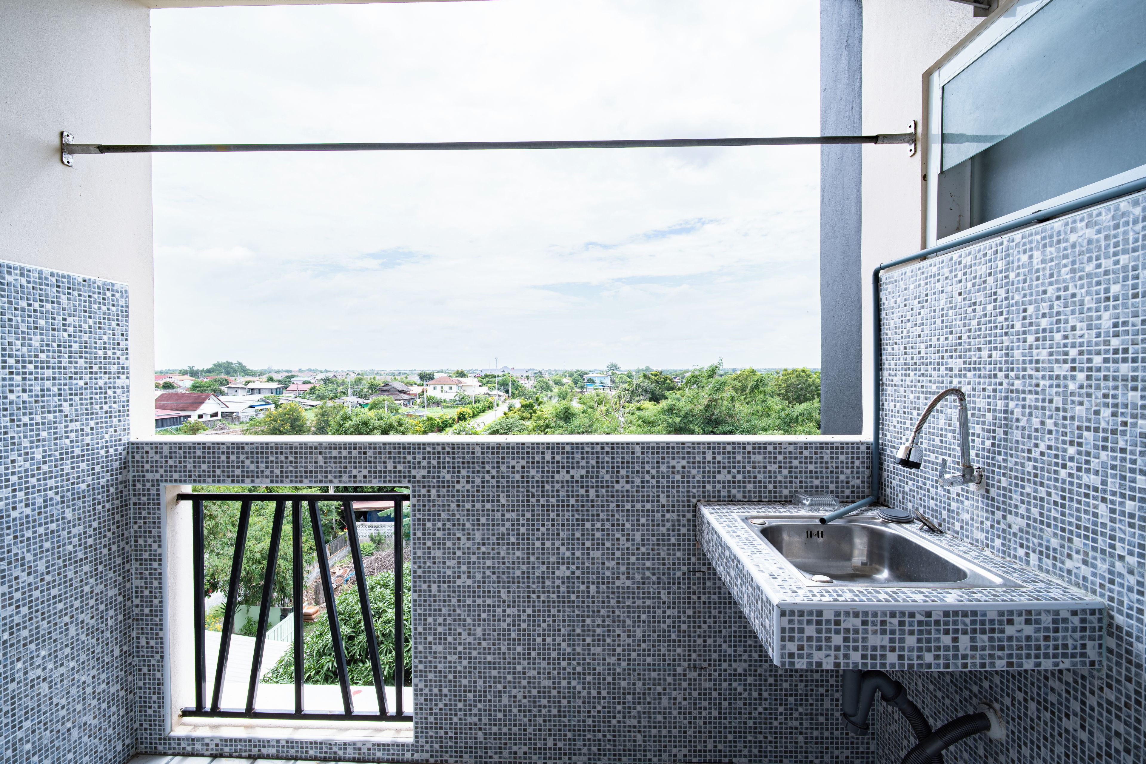 Un petit balcon donnant sur un quartier résidentiel, une fenêtre et un évier avec un robinet.