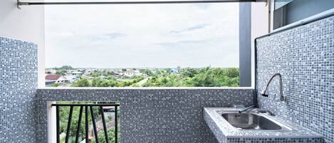 Un petit balcon donnant sur un quartier résidentiel, une fenêtre et un évier avec un robinet.