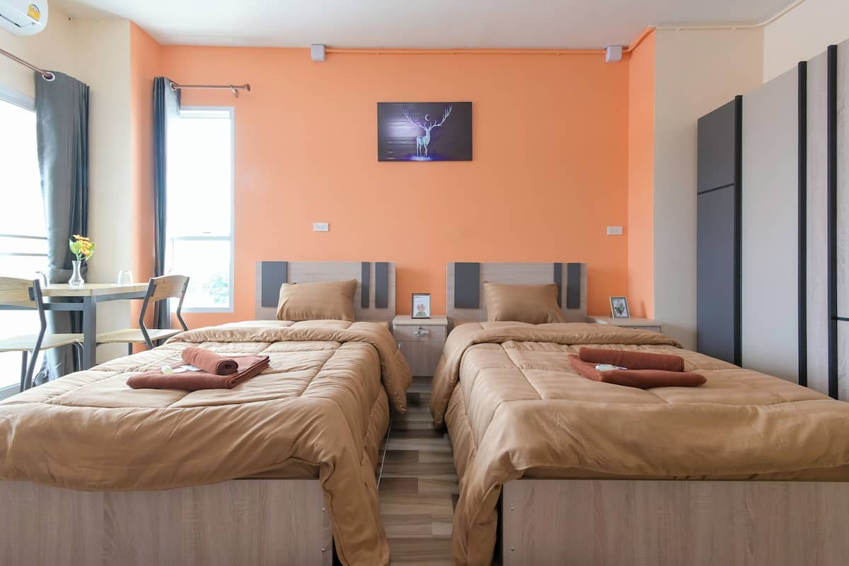 A hotel room with two beds, a desk, and a chair. There is a painting on the wall and a window with curtains.