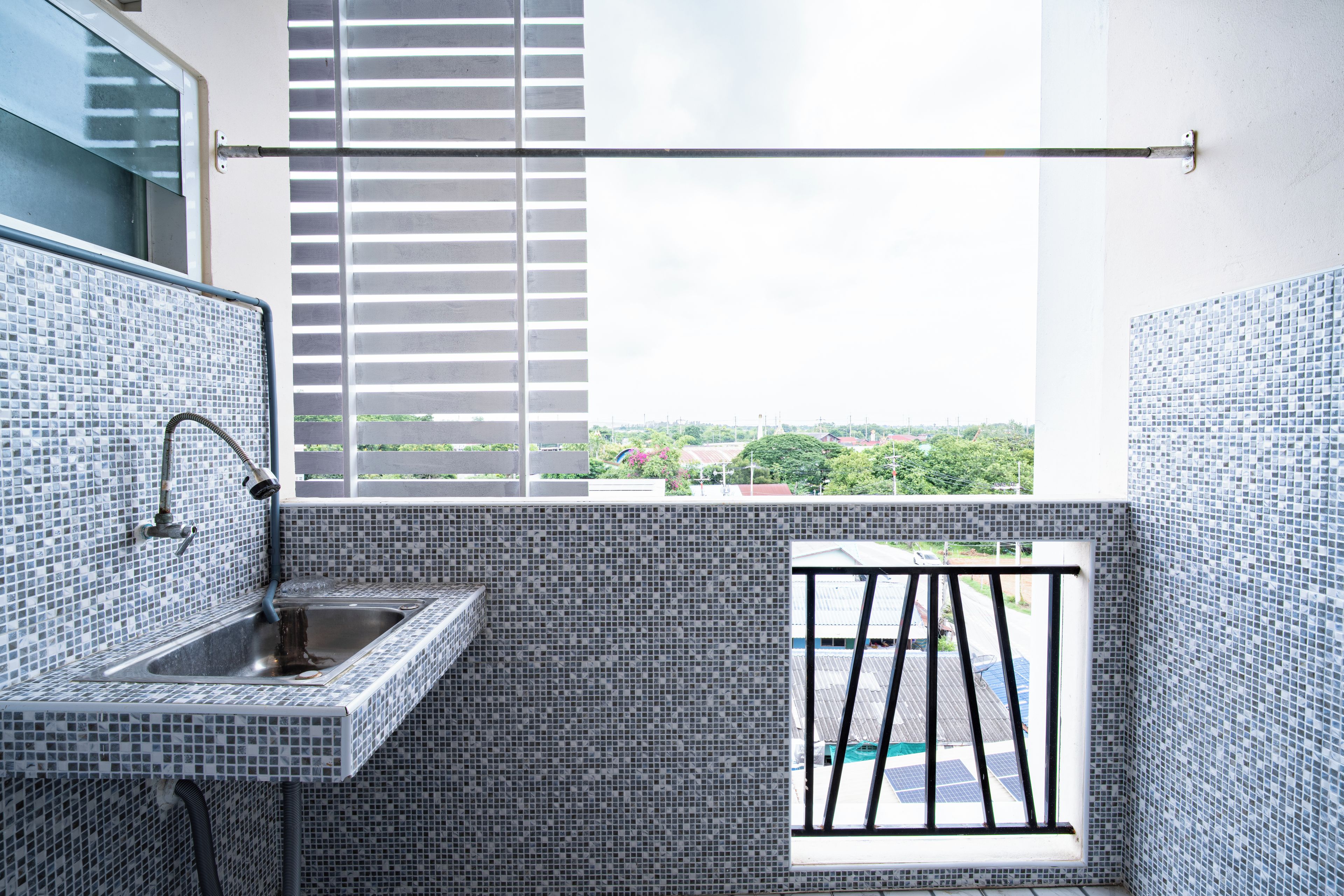 A bathroom with a tiled sink, a window with a view of the city, and a balcony with a metal railing.