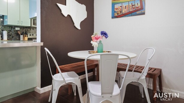 A dining area with a white table and chairs, a decorative wall piece, and a poster. - Crockett #100 xxxxxx (Austin)