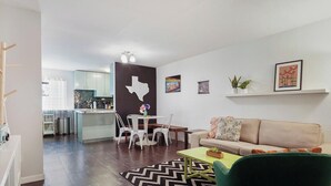 A modern living room with a sofa, a dining area with chairs, a kitchen in the background, and a Texas state outline on the wall. - Crockett #100 xxxxxx (Austin)