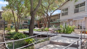 A courtyard with outdoor seating, trees, and a building with multiple windows and balconies. - Crockett #100 xxxxxx (Austin)