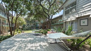 A courtyard with a wooden deck, hammocks, and a garden area with plants and trees. - Crockett #100 xxxxxx (Austin)