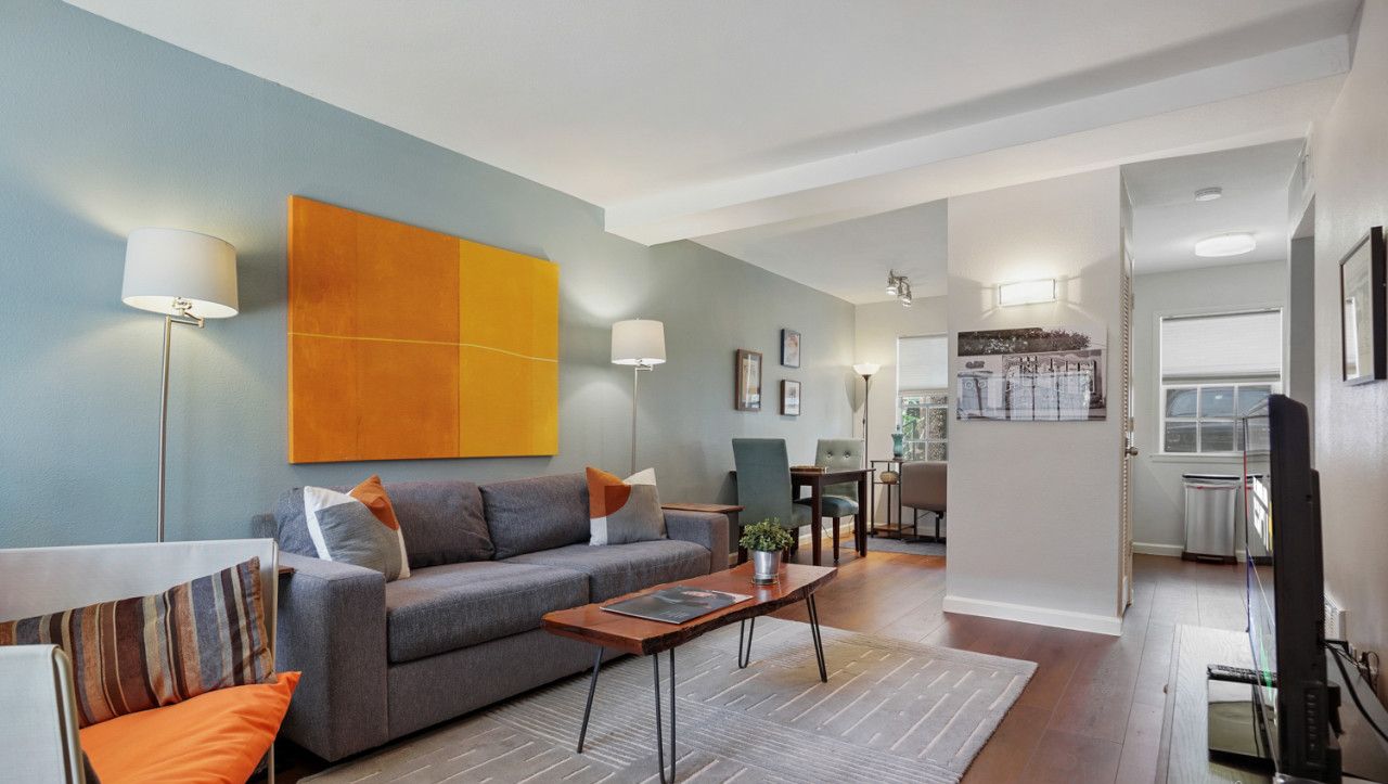 Una sala de estar moderna con un sofá gris, cojines naranja, una mesita de centro y una obra de arte naranja grande en la pared.