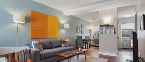 Una sala de estar moderna con un sofá gris, cojines naranja, una mesita de centro y una obra de arte naranja grande en la pared.