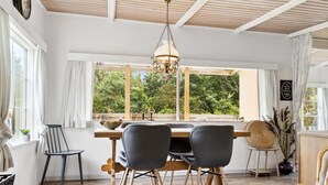 Zona pranzo con tavolo in legno, quattro sedie, lampadario e ampie finestre che si affacciano sul verde.