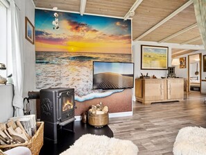 Ein gemütliches Wohnzimmer mit Kamin, einer großen Wandmalerei mit Strandmotiv und einem Holzschrank.