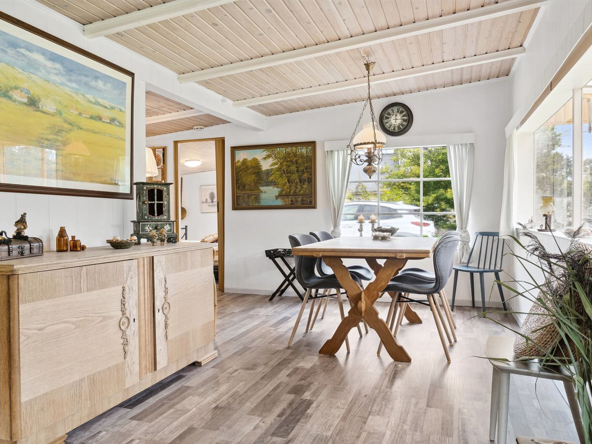 Un coin repas avec une table et des chaises en bois, un lustre et des œuvres d’art accrochées aux murs.